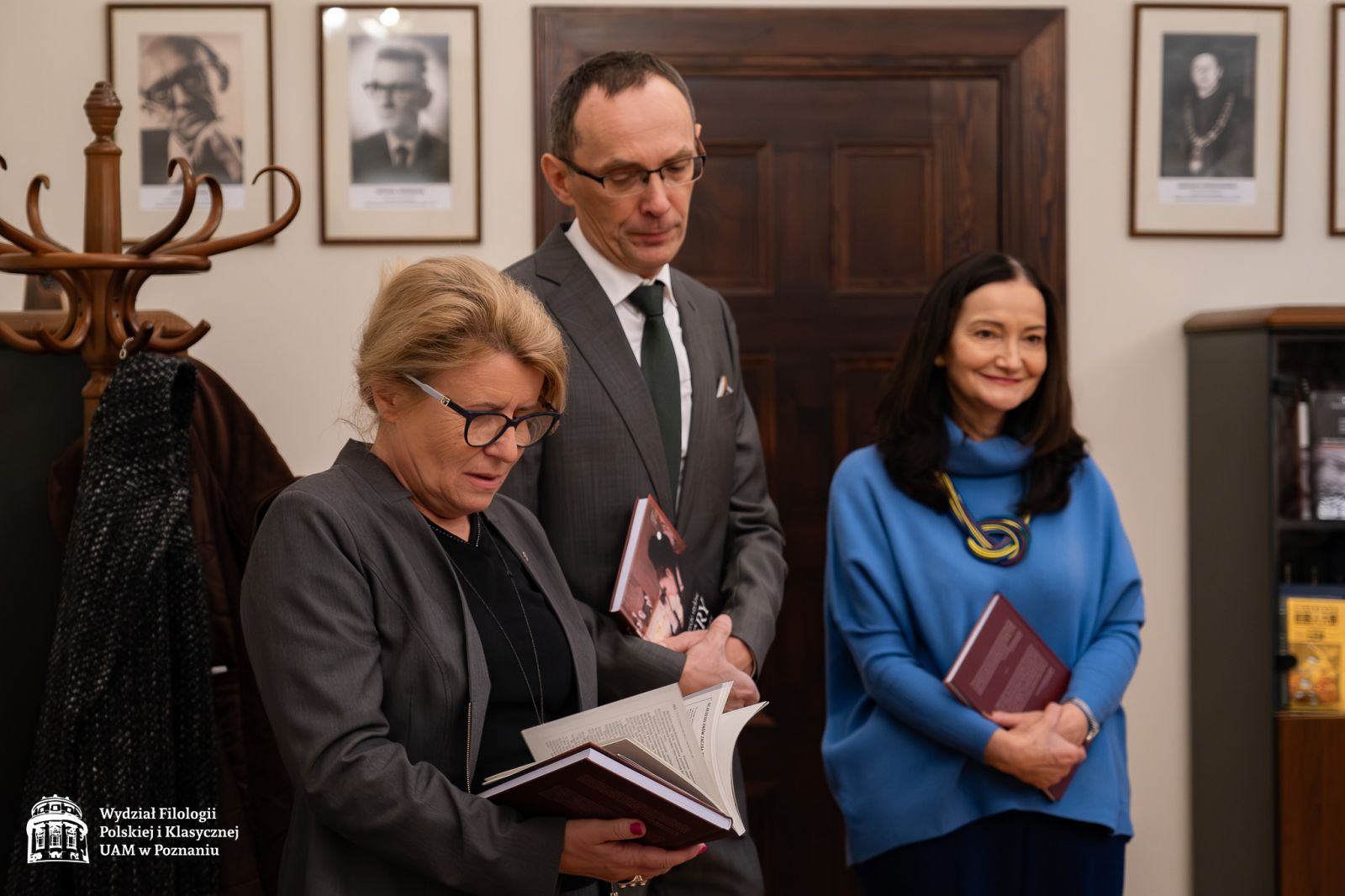 JM Rektor UAM trzyma w rękach książkę, przegląda ją, obok niej stoi prof. Grzegorz Ziółkowski i zerka jej przez ramię, dalej dr Barbara Koncewicz uśmiecha się, patrząc w bok.