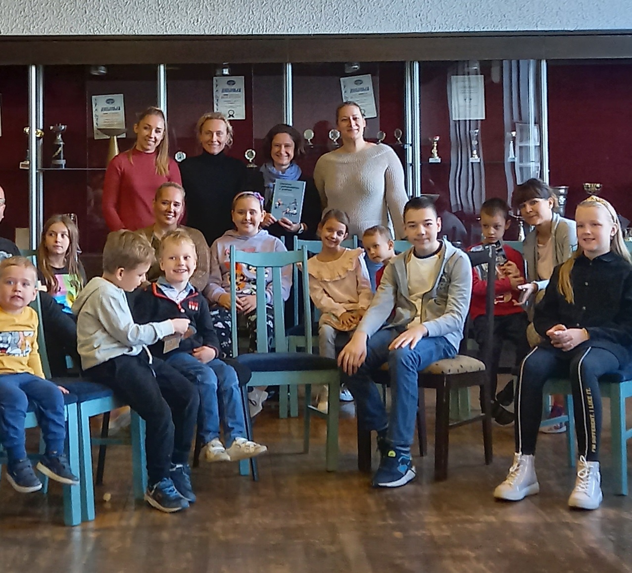 Zdjęcie grupowe uczestników zajęć w Szkole Polskiej w Belgradzie, siedzących rzędem na krzesłach i stojących w sali wykładowej.