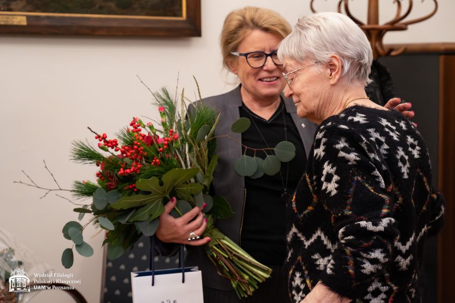 JM Rektor UAM prof. Bogumiła Kaniewska obejmuje stojącą tyłem do obiektywu prof. Dobrochnę Ratajczakową, wręczając jej bukiet kwiatów. Obie uśmiechają się do siebie.