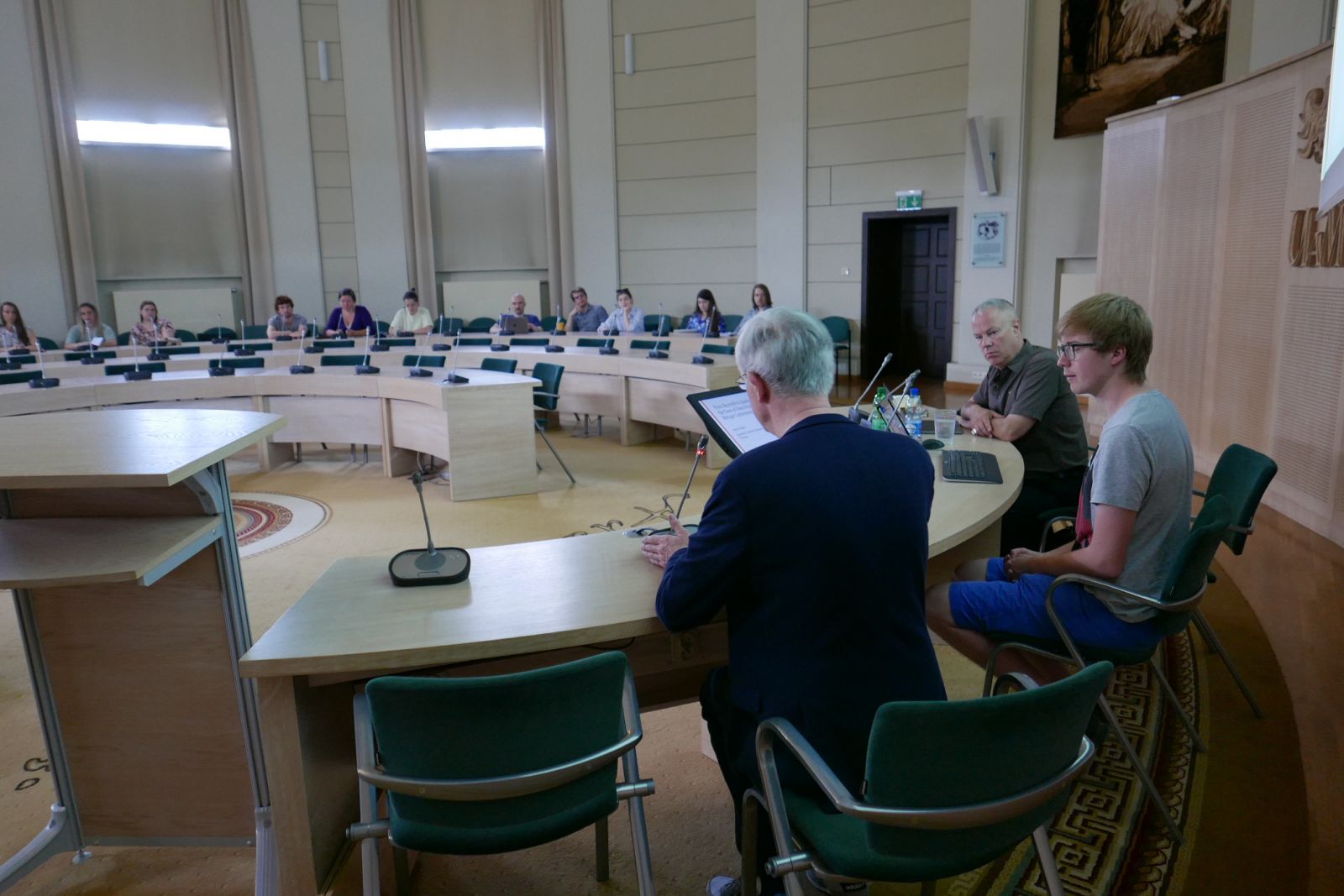 Za stołem prezydialnym w Salonie Mickiewicza siedzą: prof. Krzysztof Kozłowski, młody mężczyzna oraz prof. Anno Mungen. Zdjęcie zrobiono zza ich pleców, w tle widać słuchaczy wykładu.