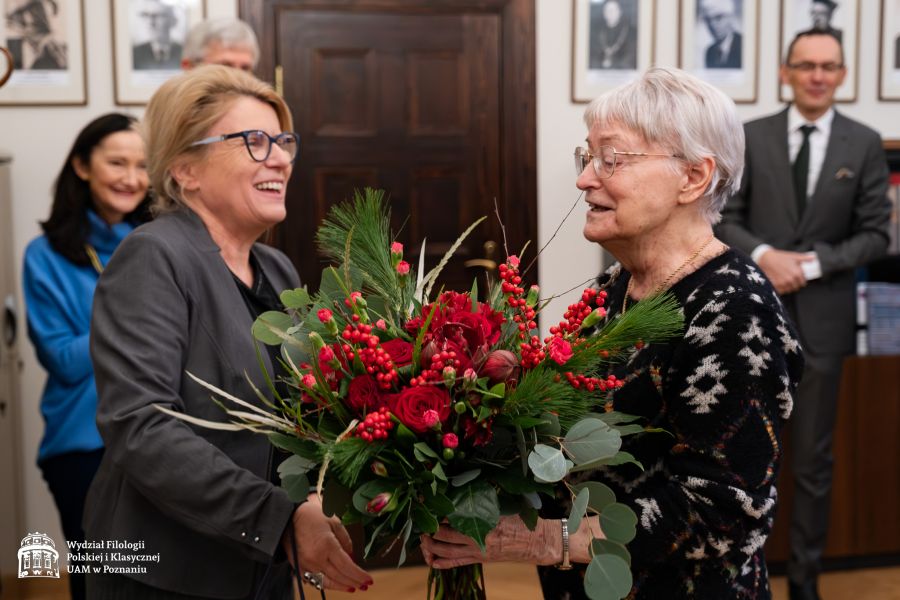 JM Rektor UAM prof. Bogumiła Kaniewska obejmuje stojącą tyłem do obiektywu prof. Dobrochnę Ratajczakową, wręczając jej bukiet kwiatów. Obie uśmiechają się do siebie.