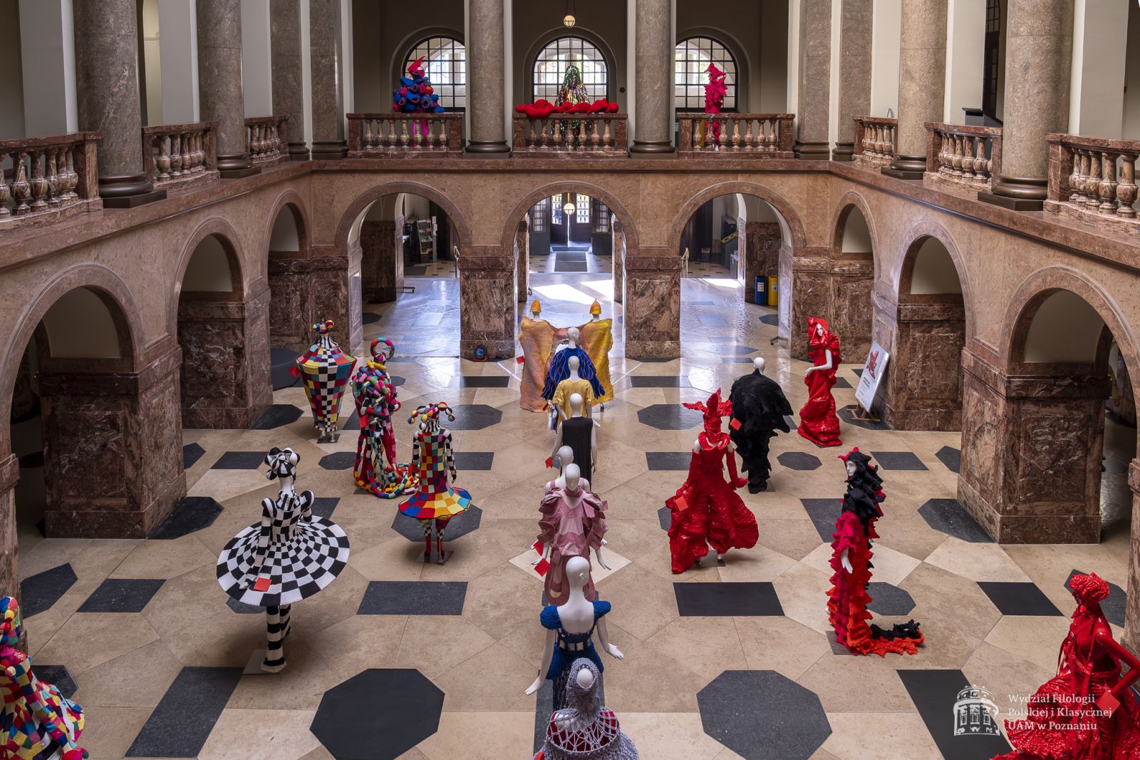 Zdjęcie manekinów w kolorowych, fantazyjnych kostiumach, stojących w holu Collegium Maius.
