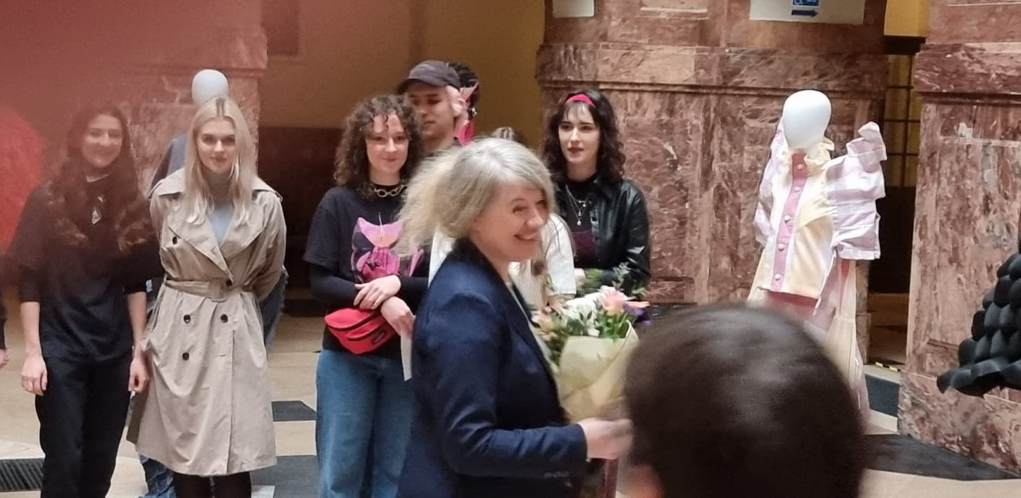 W holu głównym Collegium Maius stoi kilka osób, jedna z nich trzyma bukiet kwiatów i szeroko się uśmiecha.