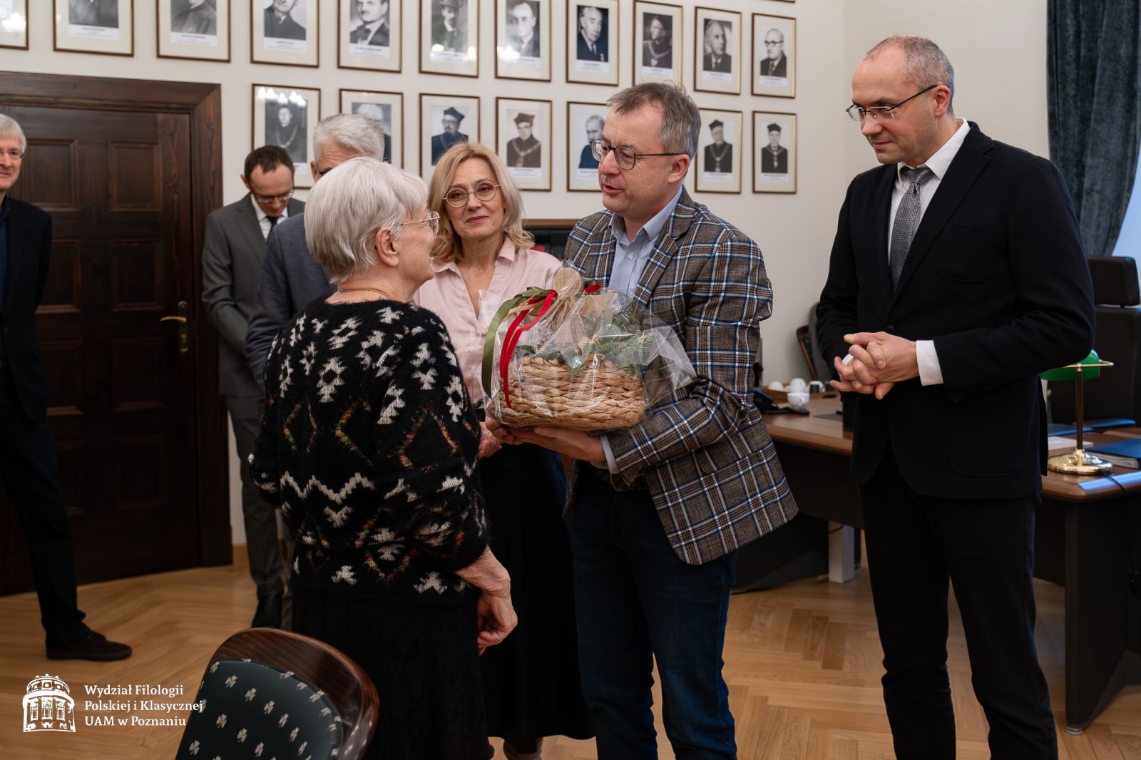 Grono dziekańskie WFPiK składa życzenia, wręcza kosz z upominkiem i kwiaty prof. Dobrochnie Ratajczakowej, wszyscy szeroko się uśmiechają.