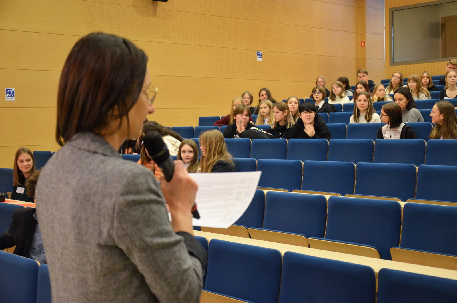 Prof. Barbara Sobczak czyta coś z kartki przez mikrofonu, stojąc przed widownią.