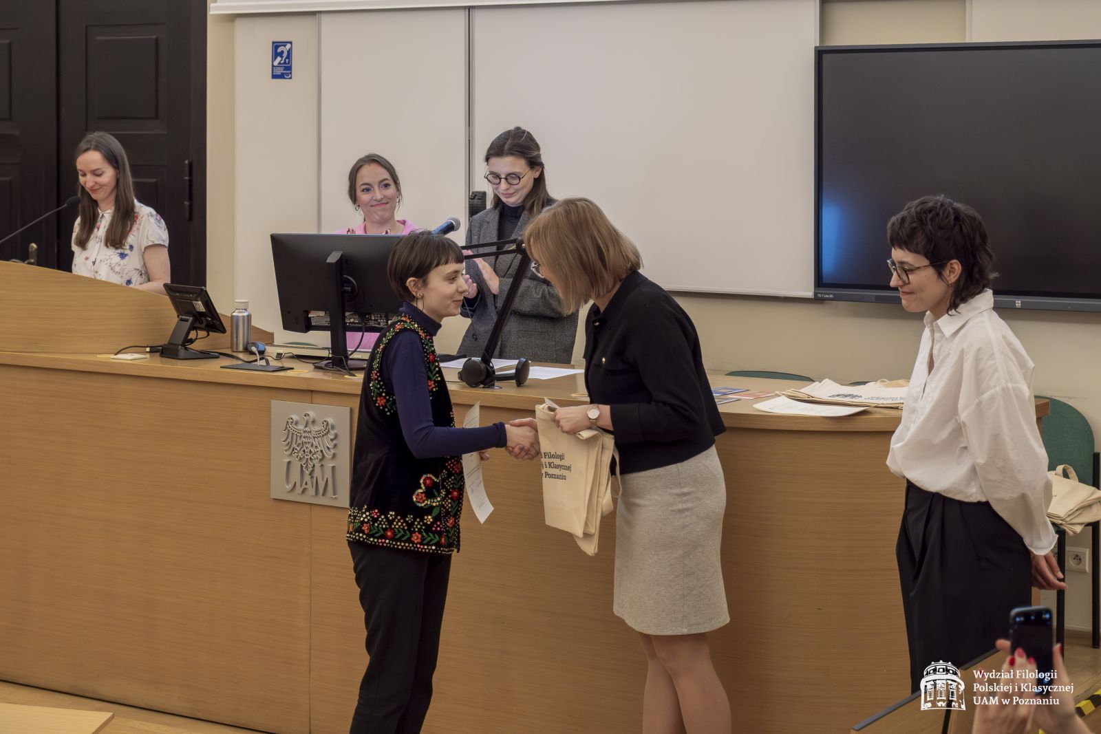 Dwie członkinie jury wręczają nagrody studentce.