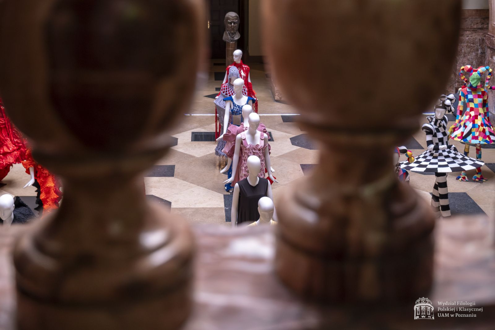 Zdjęcie manekinów w kolorowych, fantazyjnych kostiumach, stojących w holu Collegium Maius.