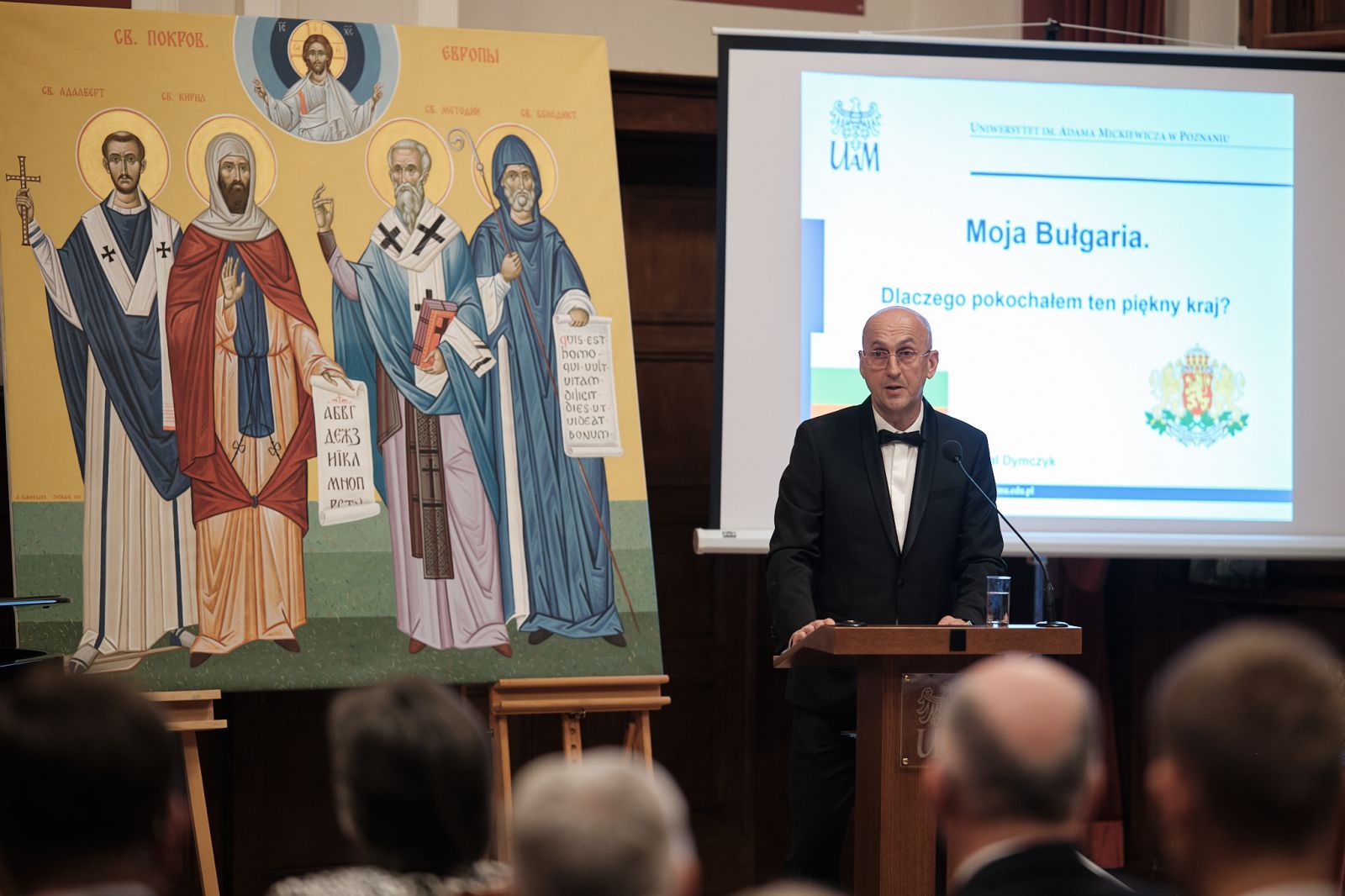 Prof. Dymczyk wygłasza przemówienie, za nim widać slajd tytułowy z prezentacji multimedialnej 