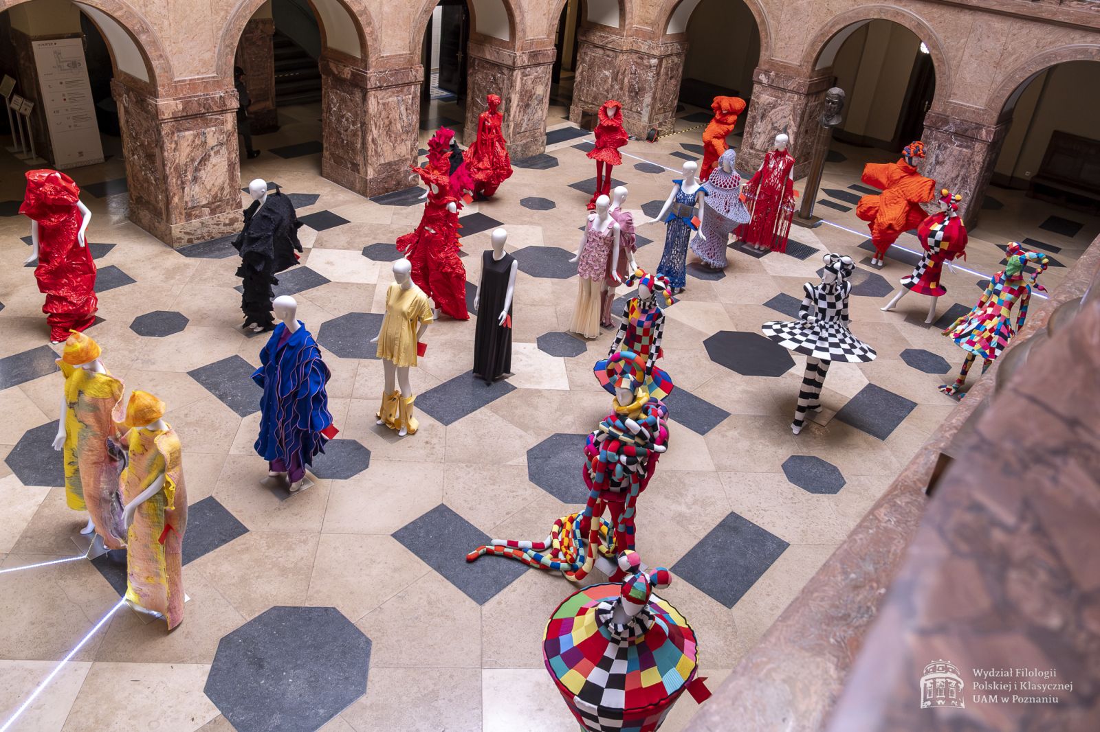 Zdjęcie manekinów w kolorowych, fantazyjnych kostiumach, stojących w holu Collegium Maius.