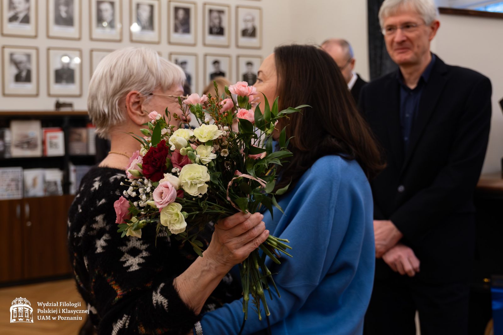 Dr Barbara Koncewicz wręcza bukiet kwiatów i ściska serdecznie prof. Dobrochnę Ratajczakową, za nią stoi uśmiechnięty prof. Krzysztof Kozłowski.