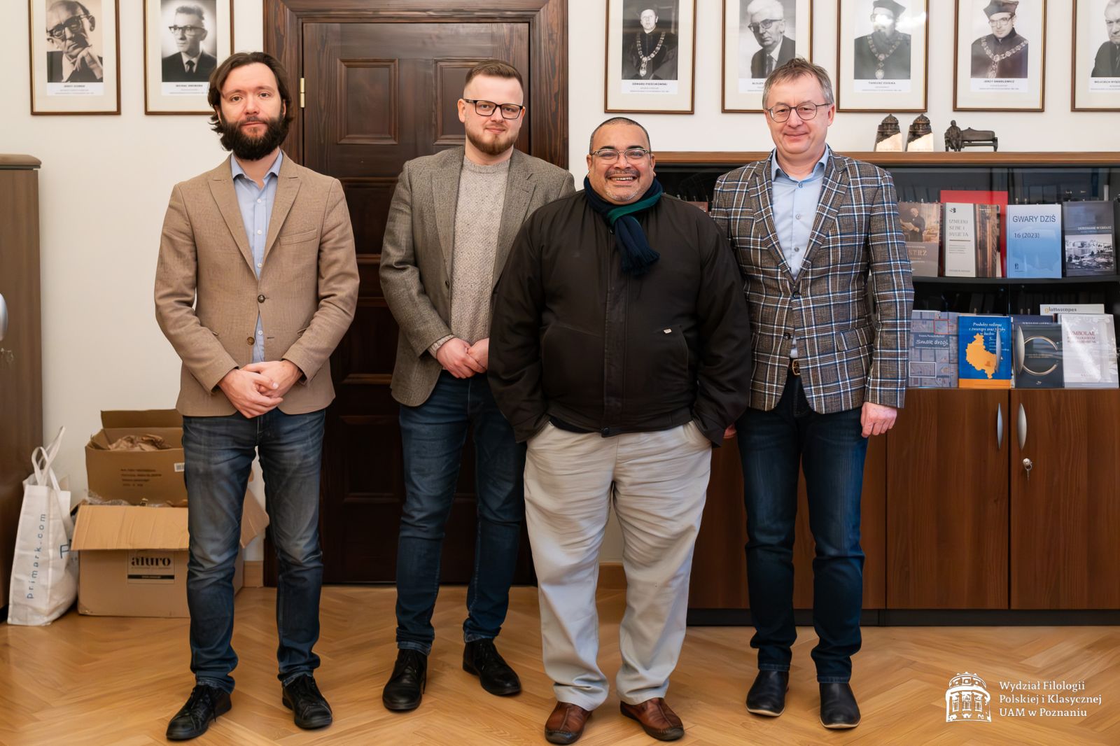 Czterech mężczyzn stoi w gabinecie Dziekana WFPiK, pozując do zdjęcia na tle portretów dawnych dziekanów.