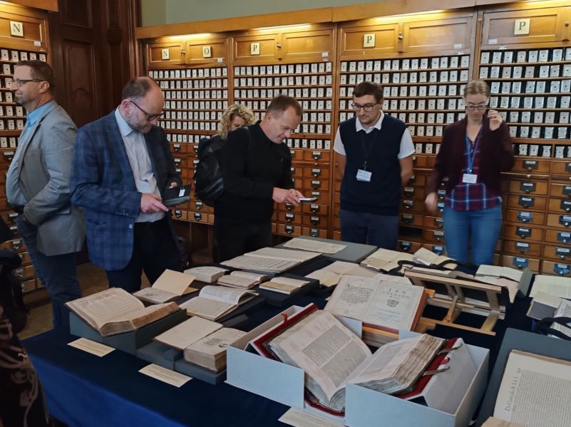 Uczestnicy Zjazdu w Bibliotece Uniwersyteckiej oglądają wystawione na stole starodruki.