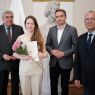 Młoda kobieta z kwiatami i dyplomem w ręku w towarzystwie trzech urzędników Miasta Poznania.