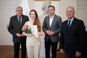 Młoda kobieta z kwiatami i dyplomem w ręku w towarzystwie trzech urzędników Miasta Poznania.