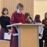 Przy mównicy w Salonie Mickiewicza stoi uczennica i odczytuje swoje wystąpienie, za nią stoją inni uczniowie i uczennice.