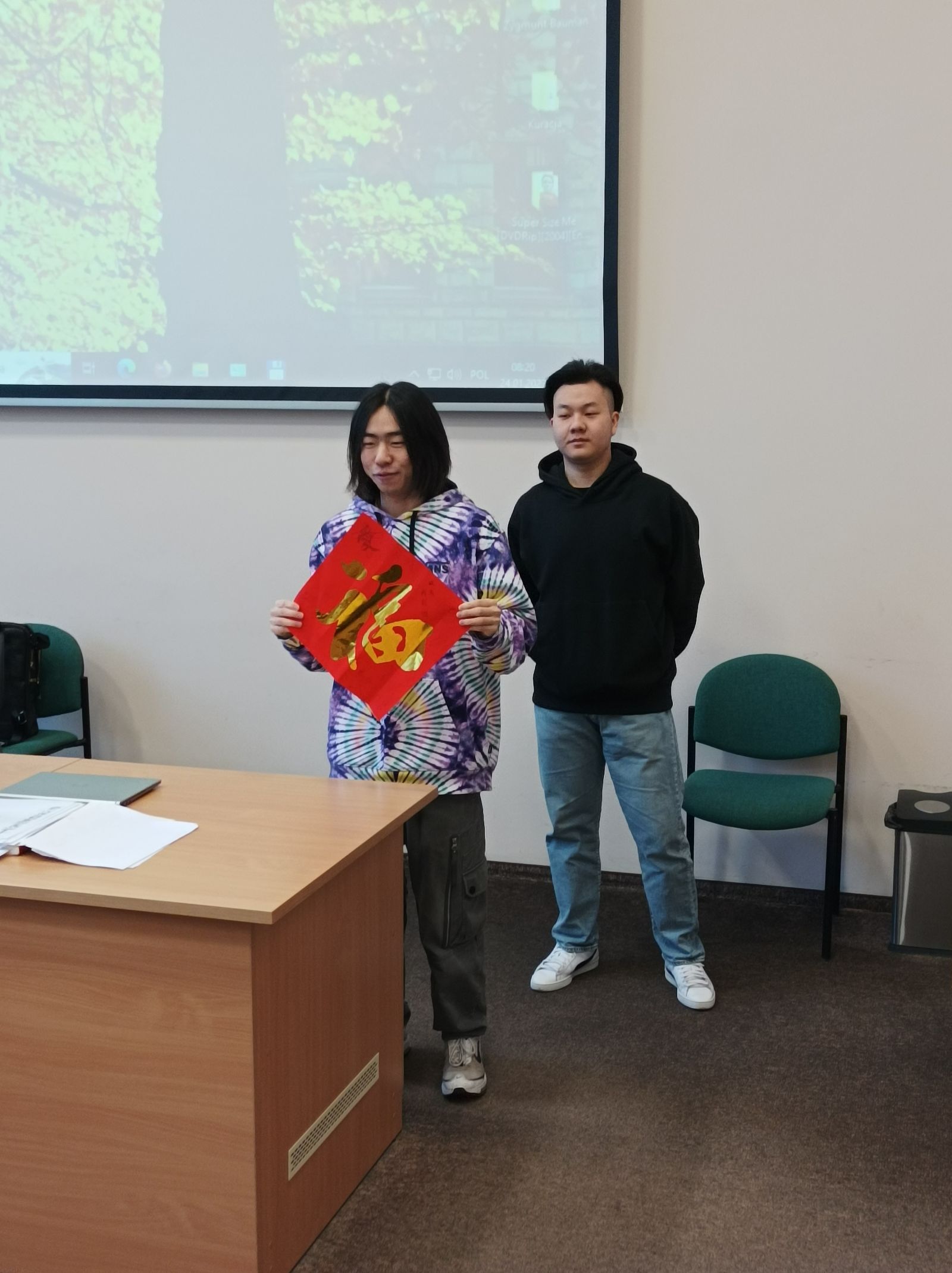 Dwaj studenci z Chin wygłaszają prezentację o chińskim Nowym roku, pokazując zebranym tradycyjną czerwoną kopertę.