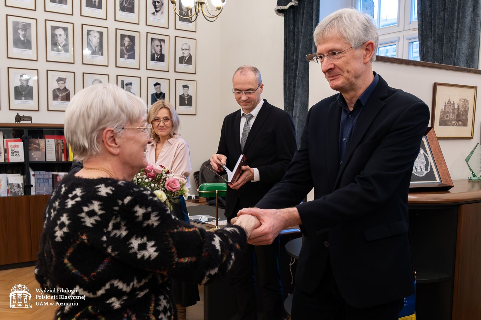 Prof. Krzysztof Kozłowski składa życzenia prof. Dobrochnie Ratajczakowej, serdecznie ściskając jej rękę obiema dłońmi, z tyłu widać prof. Krystynę Pieniążek-Marković i prof. Krzysztofa Skibskiego.