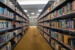 Zdjęcie regałów bibliotecznych wypełnionych książkami, stojących równolegle do siebie, tworzących głęboką perspektywę.