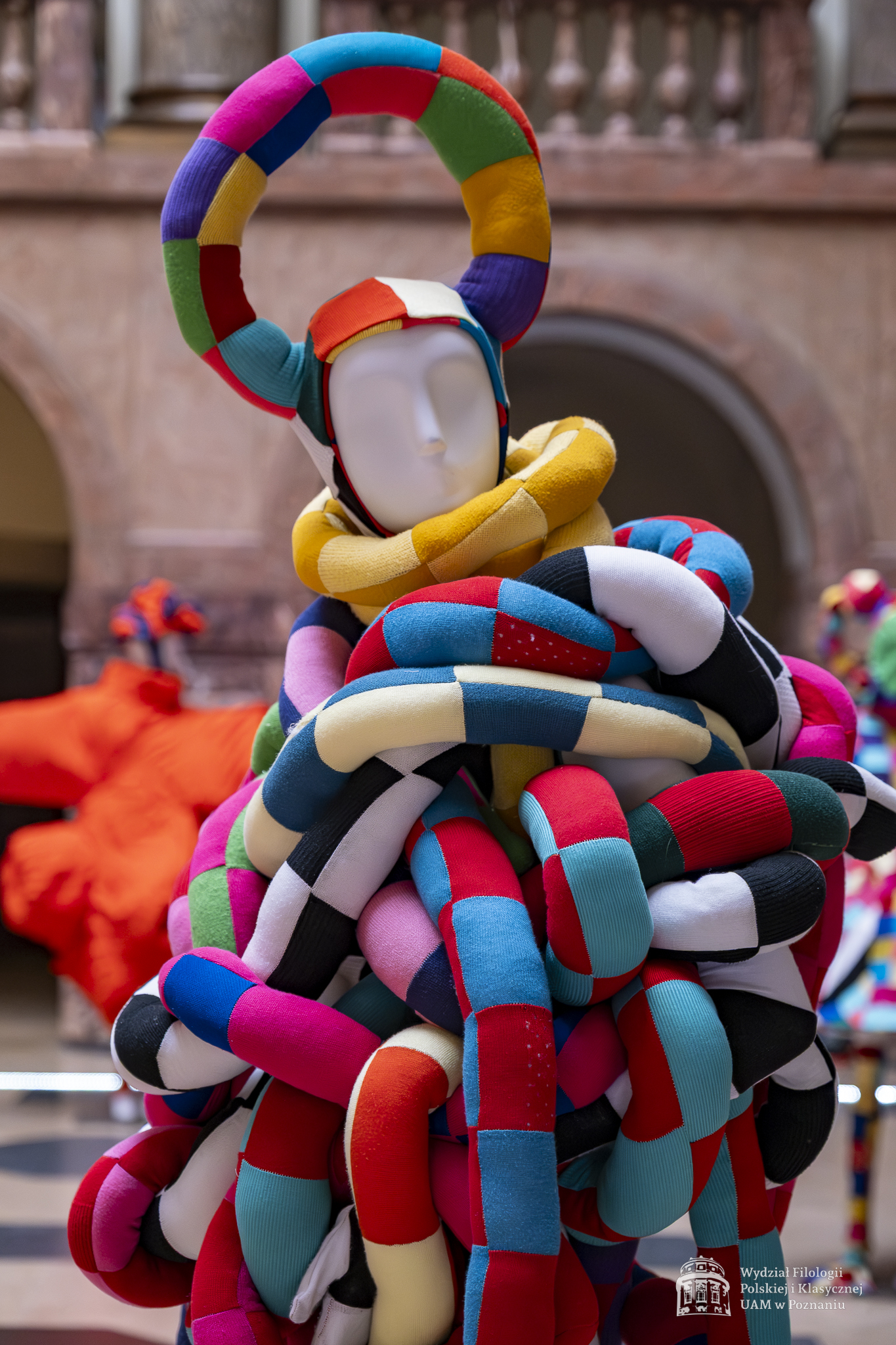 Zdjęcie manekinów w kolorowych, fantazyjnych kostiumach, stojących w holu Collegium Maius.