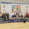 Drużyna siatkarska stoi na szczycie podium, ciesząc się z pucharu.