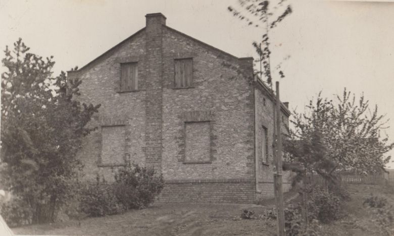 Czarno-białe zdjęcie domu z cegły z zabitymi oknami, otoczonego drzewami.