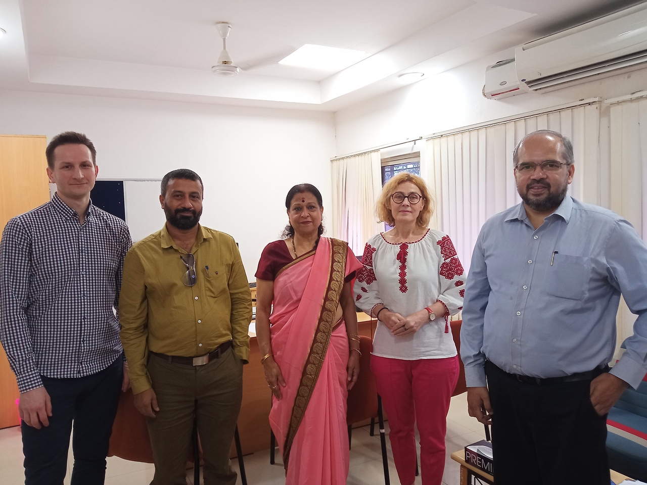 Trzech mężczyzn i dwie kobiety stoi w pomieszczeniu biurowym, jedna z kobiet jest ubrana w różowe indyjskie sari.