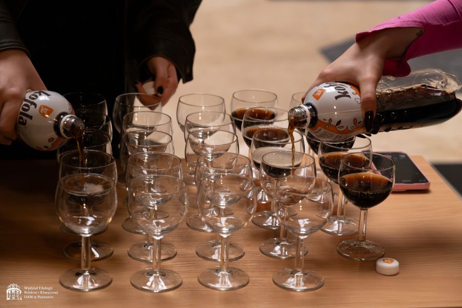Na stoliku stoją szklane kieliszki, dwie osoby, których twarzy nie widać nalewają do nich czeski, kultowy napój 