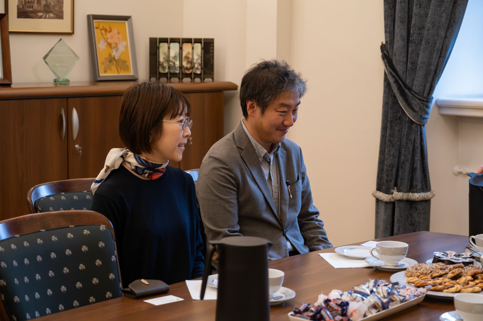 Goście z Japonii siedzą przy stole w gabinecie dziekańskim, przed nimi filiżanki z kawą i słodkości.