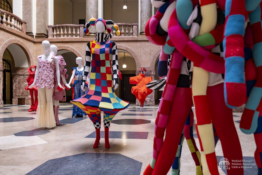 Zdjęcie manekinów w kolorowych, fantazyjnych kostiumach, stojących w holu Collegium Maius.
