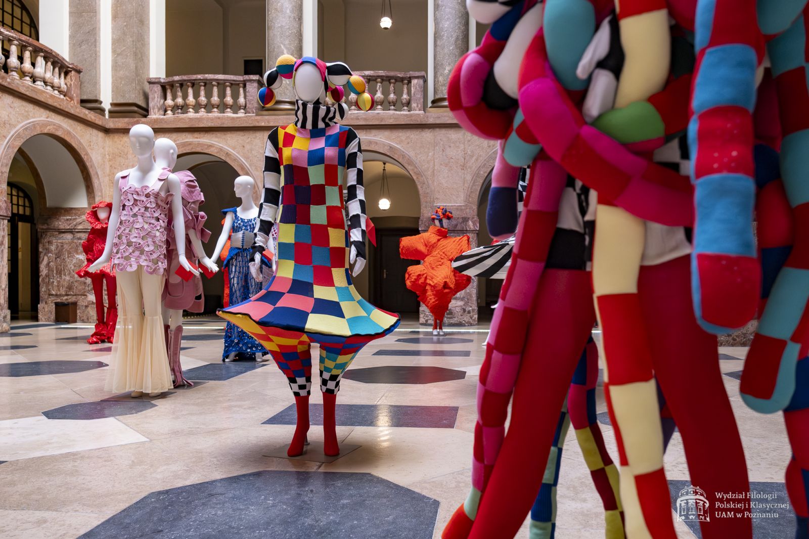 Zdjęcie manekinów w kolorowych, fantazyjnych kostiumach, stojących w holu Collegium Maius.