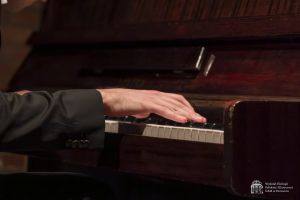 Zbliżenie na dłonie pianisty nad klawiaturą.