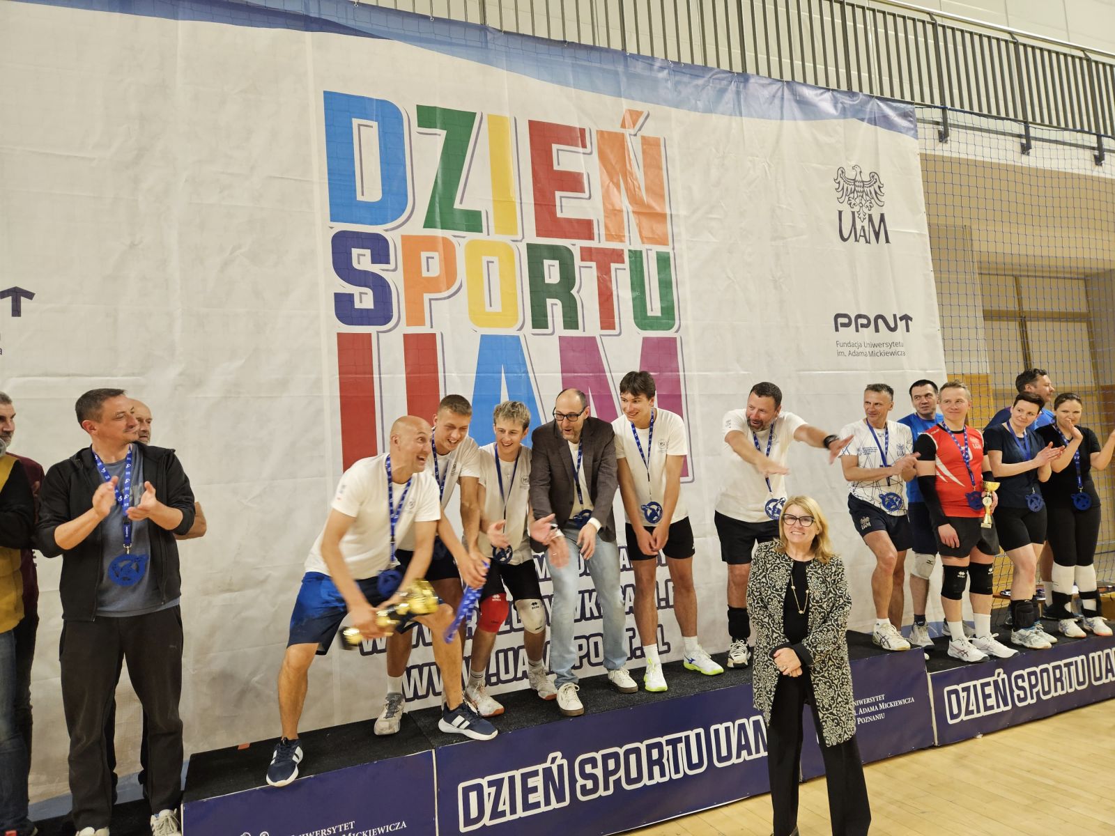 Drużyna siatkarska stoi na szczycie podium, ciesząc się z pucharu.