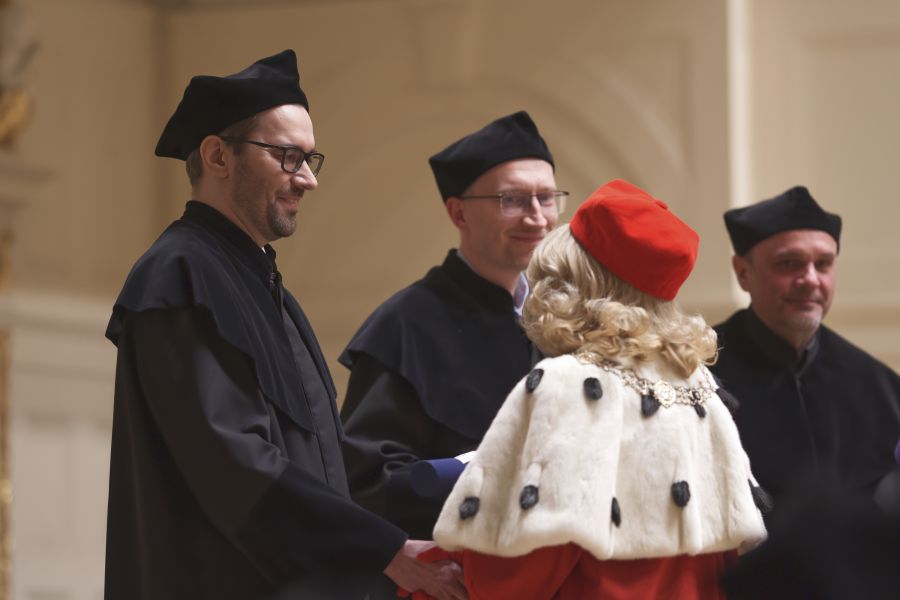 Rektor Bogumiła Kaniewska ściska dłoń prof. Błażeja Warkockiego, obok niego stoją jeszcze dwaj mężczyźni, wszyscy ubrani w czarne togi i czapki.