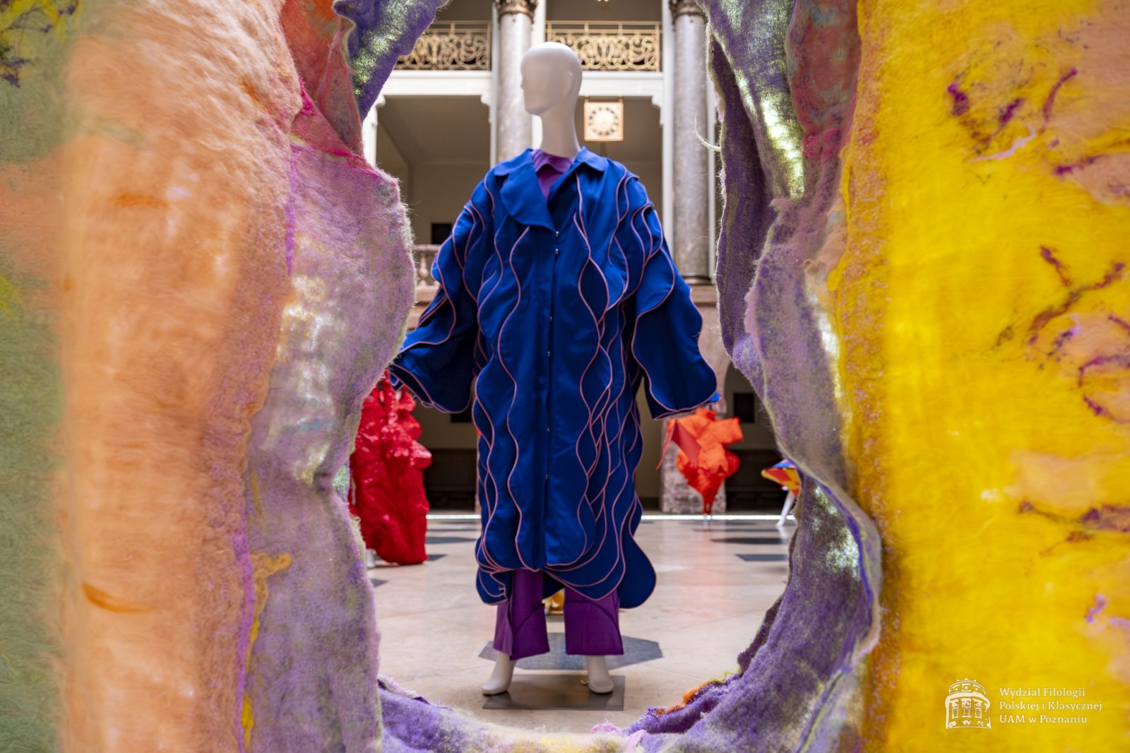 Zdjęcie manekinów w kolorowych, fantazyjnych kostiumach, stojących w holu Collegium Maius.