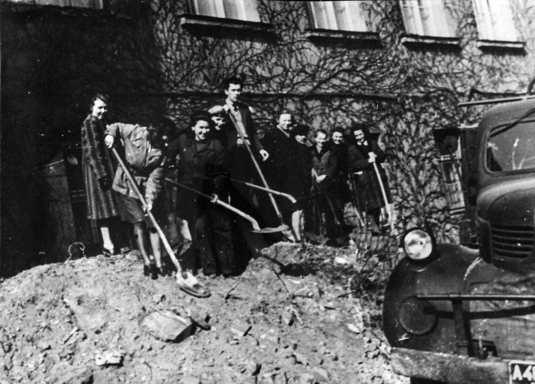 Czarno-białe zdjęcie grupy osób usuwających gruzy z ulicy miasta.
