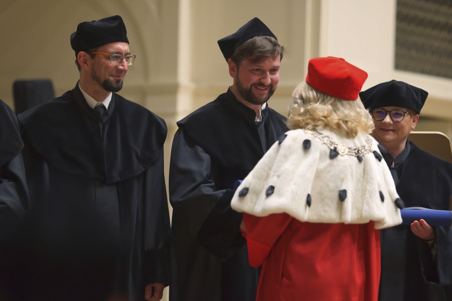 Rektor Bogumiła Kaniewska ściska dłonie osobom w czarnych togach i czapkach.