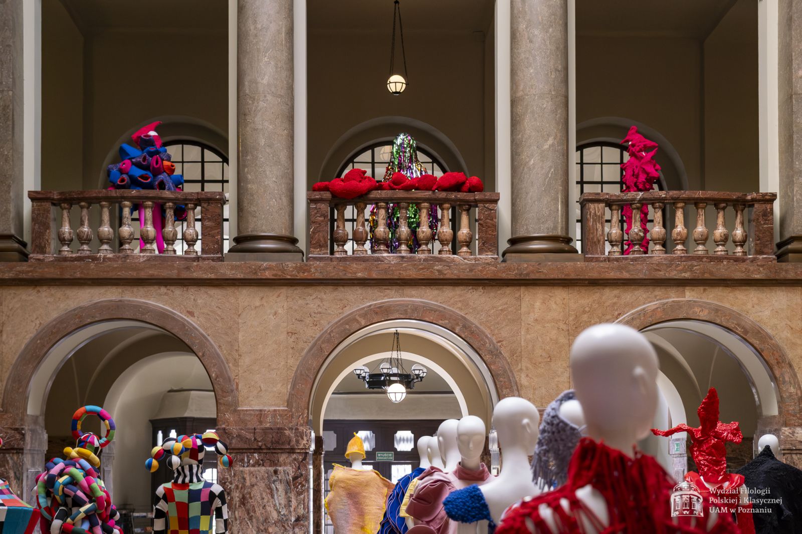 Zdjęcie manekinów w kolorowych, fantazyjnych kostiumach, stojących w holu i na pierwszym piętrze Collegium Maius.