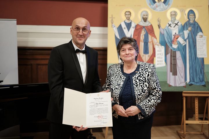 Nowy konsul i Ambasador Bułgarii prezentują do obiektywu akt mianowania, za nimi na sztalugach stoi prawosławna ikona.