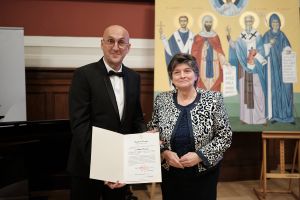 Nowy konsul i Ambasador Bułgarii prezentują do obiektywu akt mianowania, za nimi na sztalugach stoi prawosławna ikona.