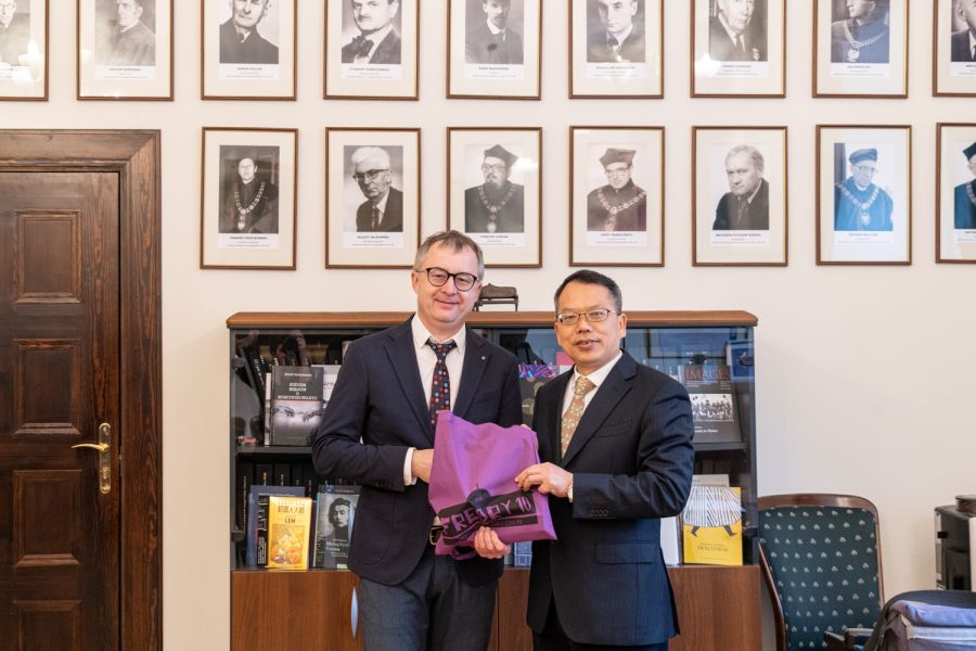 Na tle portretów dawnych dziekanów WFPiK stoi Dziekan Mizerkiewicz oraz gość z Chin, obaj trzymają fioletową torbę z logo Fredry 10.