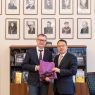 Na tle portretów dawnych dziekanów WFPiK stoi Dziekan Mizerkiewicz oraz gość z Chin, obaj trzymają fioletową torbę z logo Fredry 10.
