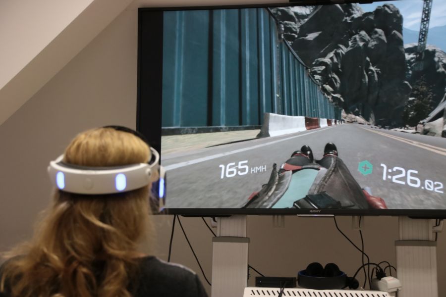 Uczestniczka warsztatów w okularach do VR gra w grę komputerową, która wyświetla się na ekranie telewizora.