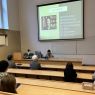 W sali wykładowej z rzędami pnących się ławek widać wyświetloną prezentację, a poniżej prelegentkę - prof. Hikaru Ogurę