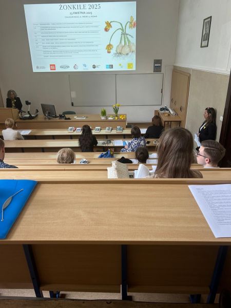 Zdjęcie z górnych rzędów ławek w sali Kuraszkiewicza, w których siedzą uczestnicy czytania, na dole wyświetla się prezentacja z programem wydarzenia, a przy mównicy stoi prof. Katarzyna Kuczyńska-Koschany,