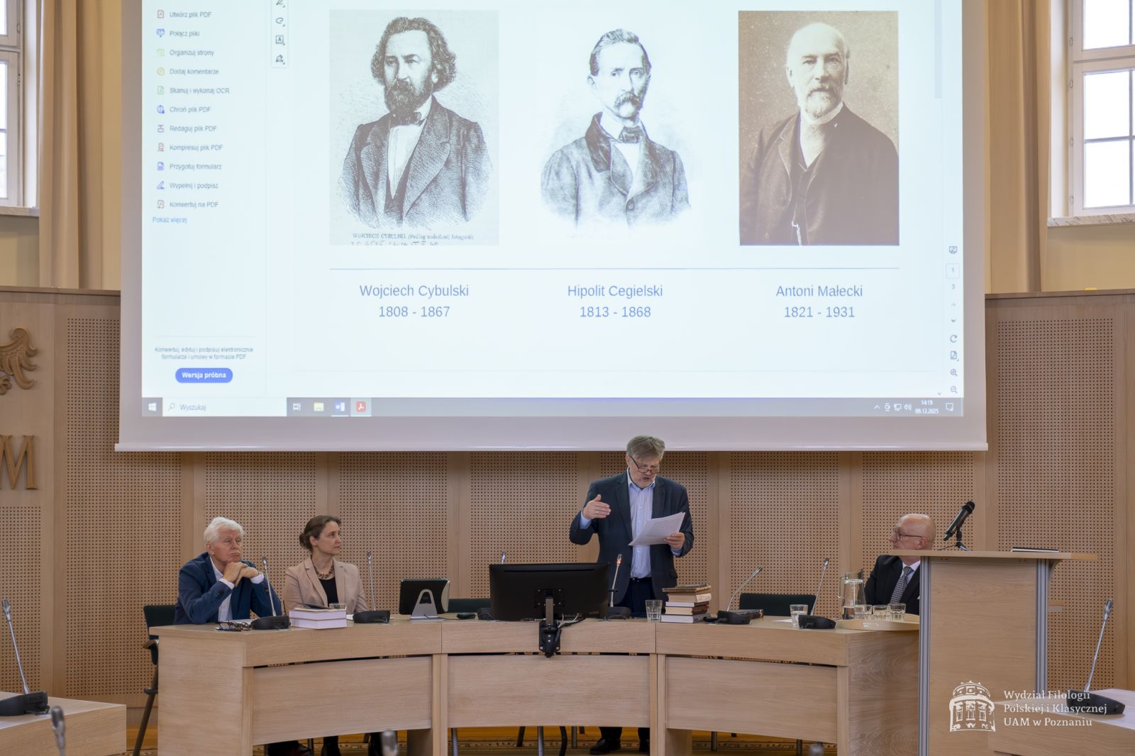 Prof. Fiećko wygłasza swój referat w Salonie Mickiewicza, nad nim na ekranie wyświetlają się portrety Wojciecha Cybulskiego, Hipolita Cegielskiego i Antoniego Małeckiego.