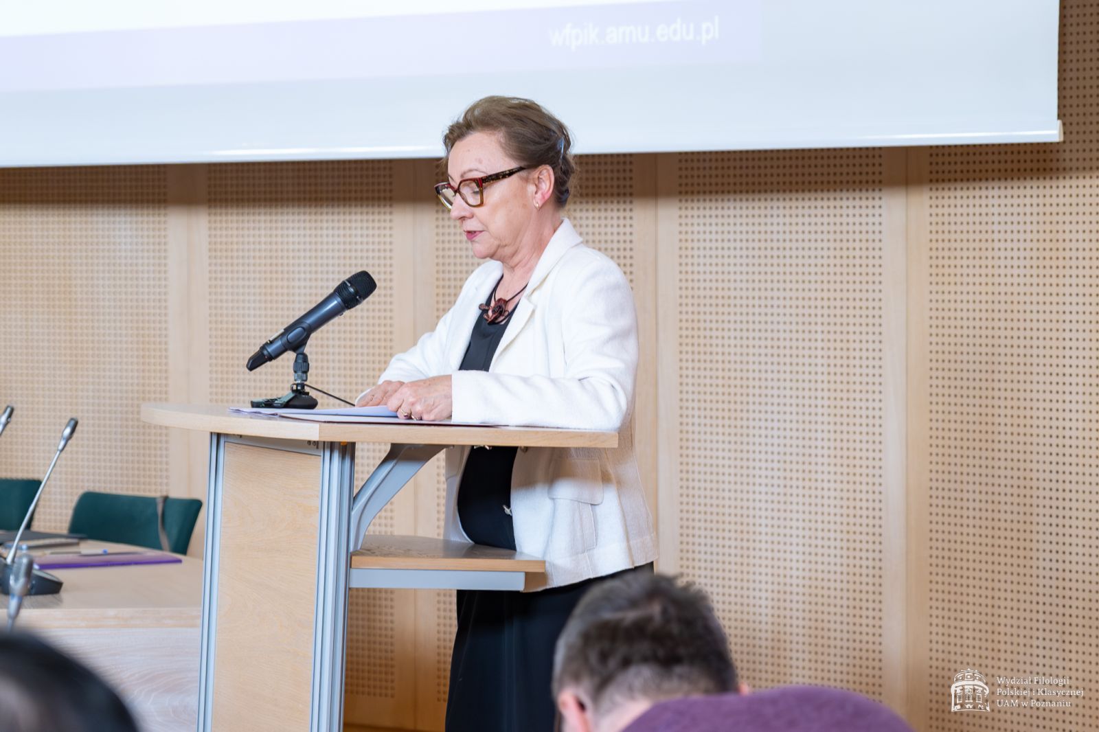 Prof. Mariola Mikołajczak odczytuje werdykt, stojąc przy mównicy w Salonie Mickiewicza.