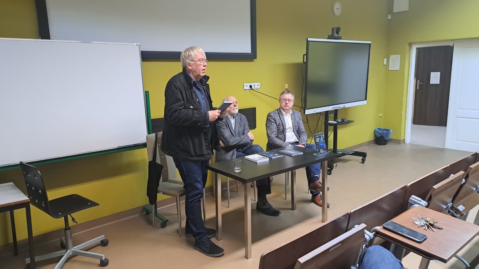 Goście spotkania promującego nowe wydanie tomiku Jana Kaspra, wydawca stoi, prezentując książkę.