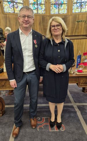 Prof. Tomasz Mizerkiewicz stoi obok JM Rektor UAM prof. Bogumiły Kaniewskiej w gabinecie rektorskim, dumnie prezentując medal KEN wpięty w marynarkę.