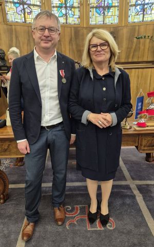 Prof. Tomasz Mizerkiewicz stoi obok JM Rektor UAM prof. Bogumiły Kaniewskiej w gabinecie rektorskim, dumnie prezentując medal KEN wpięty w marynarkę.