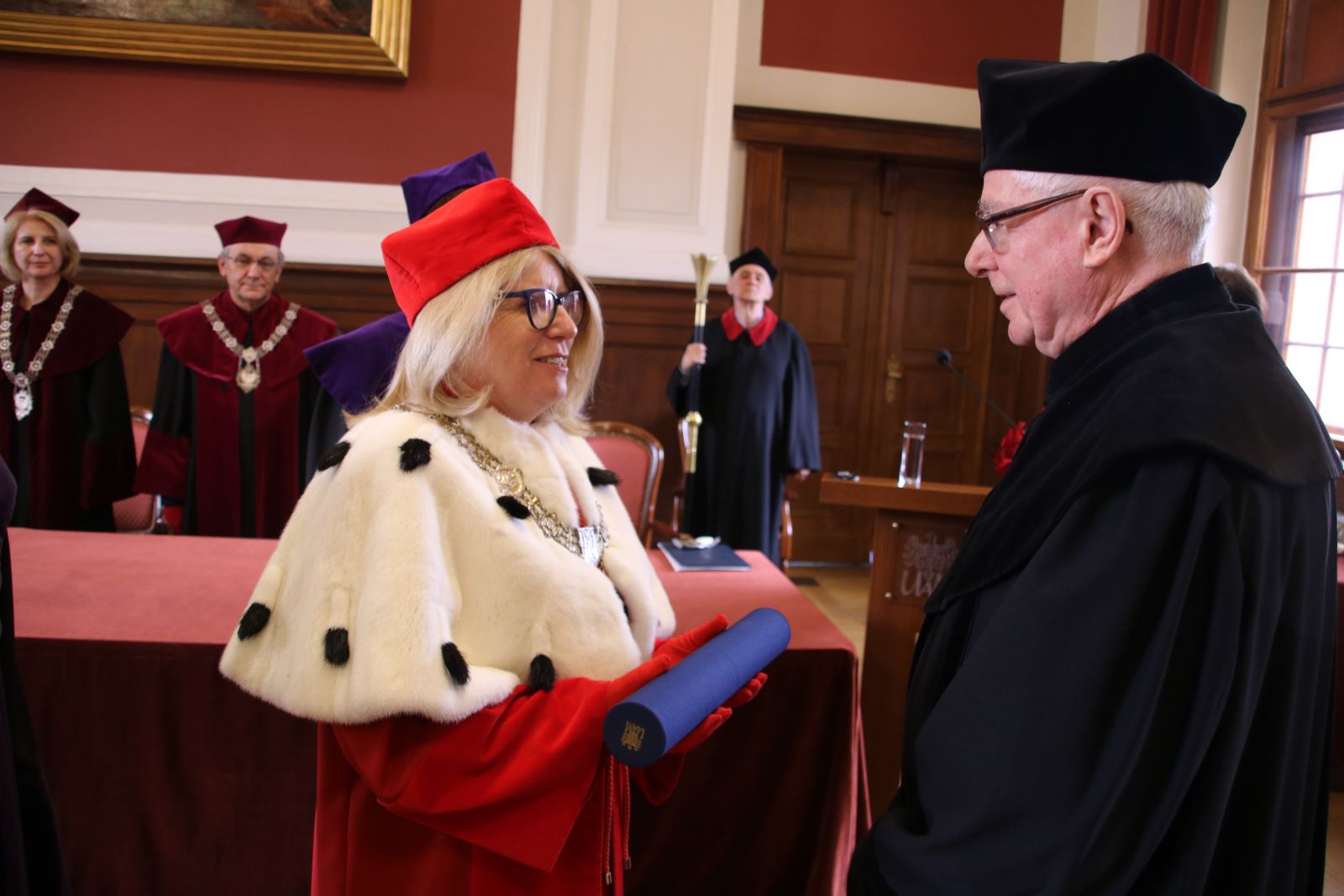 Rektor UAM wręcza dyplom doktorski prof. Danielewiczowi. Jest ubrana w czerwoną togę, czerwony biret i płaszcz z gronostajów.